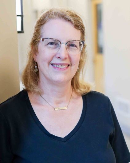 Smiling woman in glasses wearing a black top in a softly lit indoor hallway
