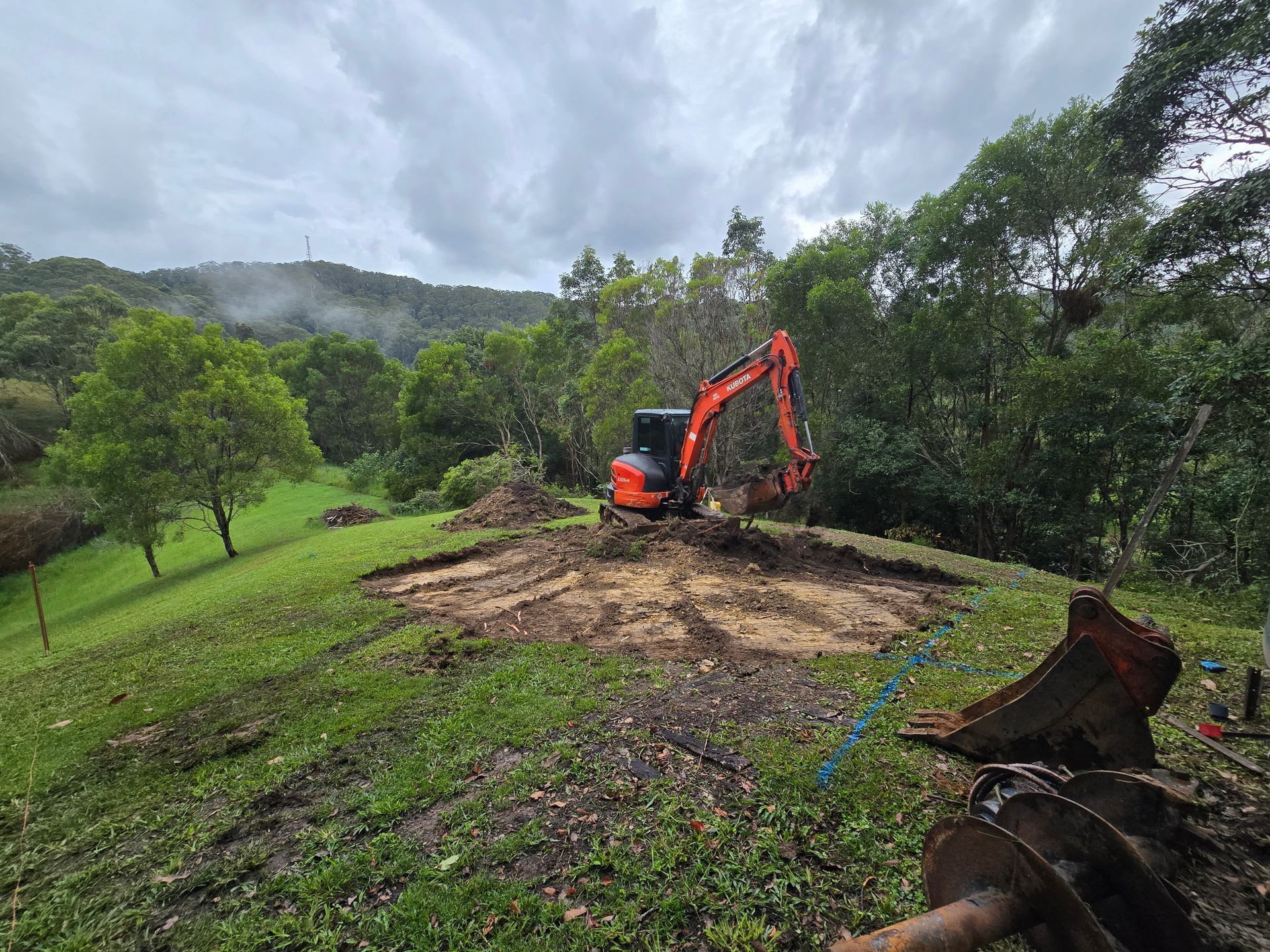 A Blue Excavator is Parked on the Side of a Road — TJ Concreting in Northern Rivers, NSW