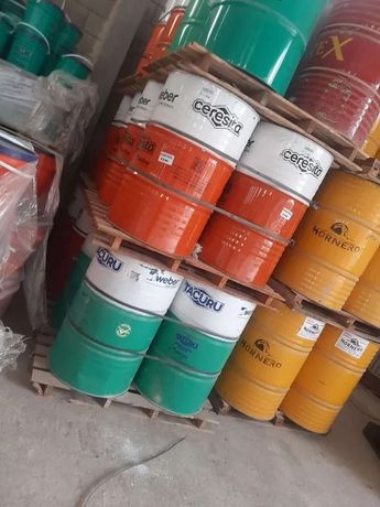 Cubos de pintura metálicos apilados en colores verde, naranja, amarillo y turquesa dentro de un escaparate.