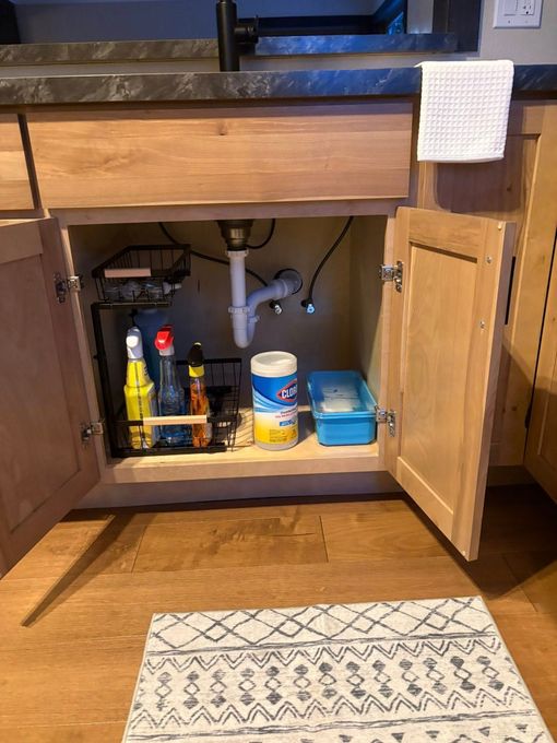 Open bathroom vanity cabinet with cleaning supplies, pipes, and a hand towel on the sink edge.
