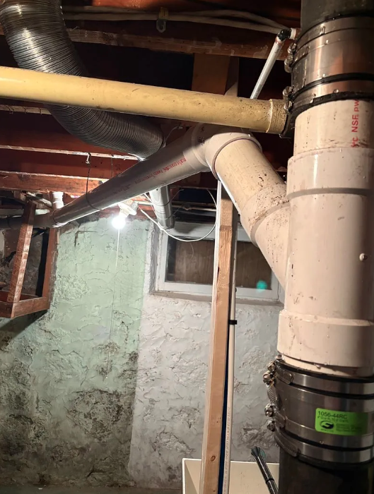 Basement ceiling with exposed ducts and pipes against a concrete wall and small window.