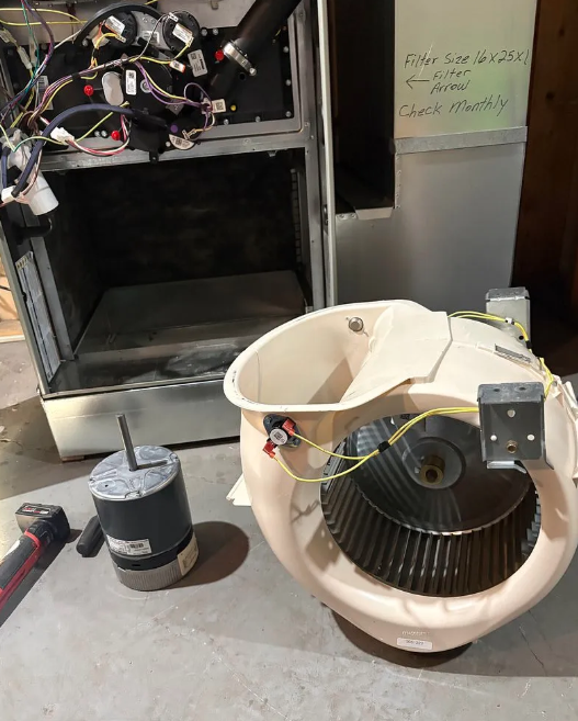 Disassembled HVAC blower housing and motor parts on a concrete floor in a workshop.