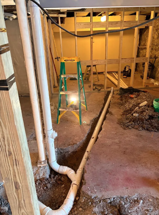 Bathroom under renovation with exposed framing, plumbing pipes, and a green step ladder.