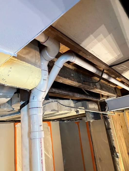 Exposed ceiling pipes and ducts in a basement or crawl space with insulation and wooden beams