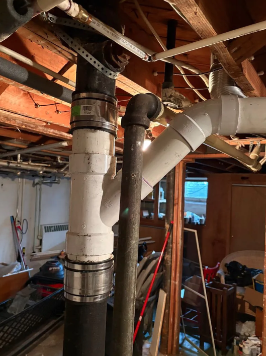Basement with exposed wooden beams and white duct and vent pipes running through unfinished ceiling