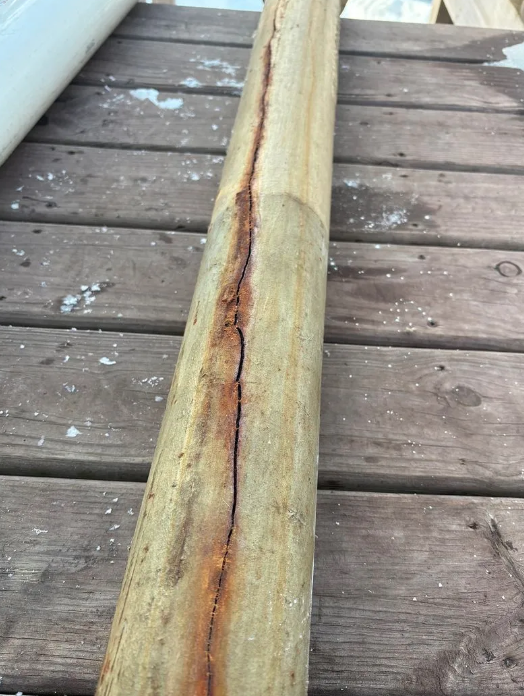 Cracked wooden pole lying on a weathered deck, with a dark split running down the center.