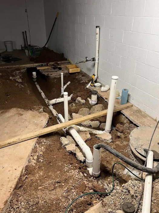 Exposed plumbing pipes and drain lines in a concrete basement floor under construction.