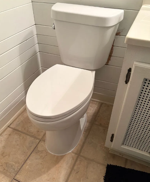 White toilet in a tiled bathroom beside a cabinet and tan floor tiles