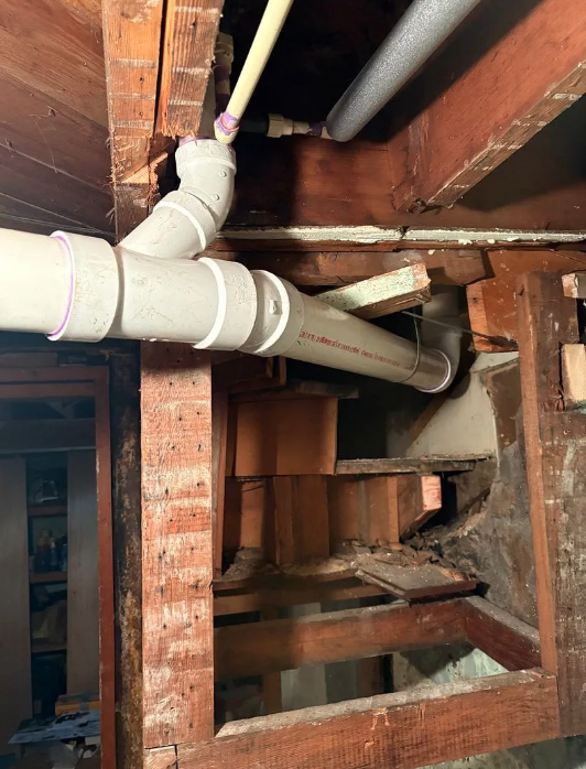 Open ceiling with white PVC pipes running through exposed wooden framing and brick walls