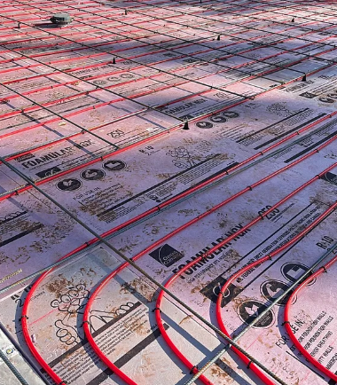 Pink insulation boards with red tubing laid out on a floor for radiant heating installation