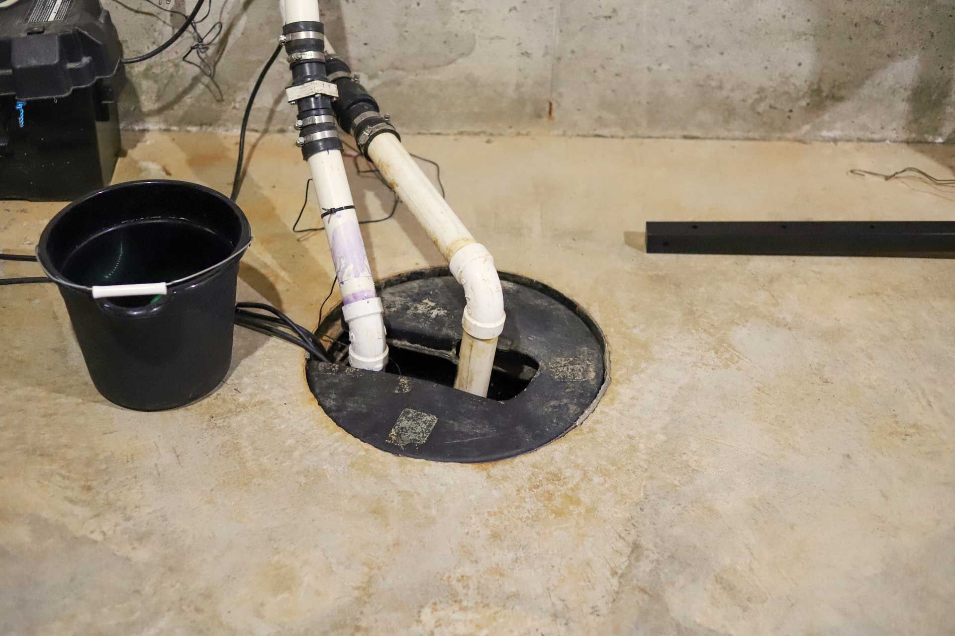 A sump pump in a concrete floor, with black bucket, white and black pipes. A sump pump in a concrete floor, with black bucket, white and black pipes.