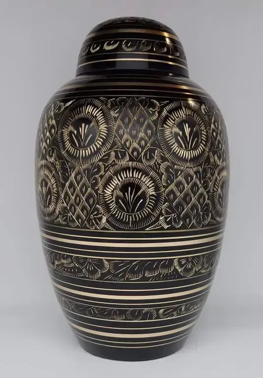 A black vase with a gold pattern on it is sitting on a white surface.