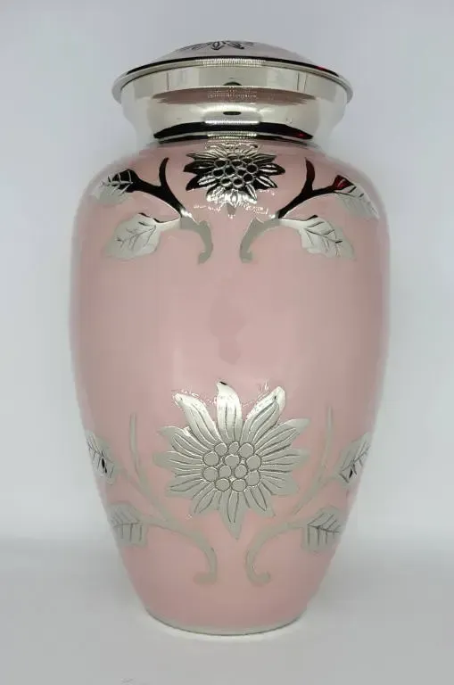 A pink vase with a silver flower on it is on a white surface.
