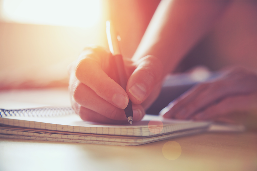 A person is writing in a notebook with a pen.