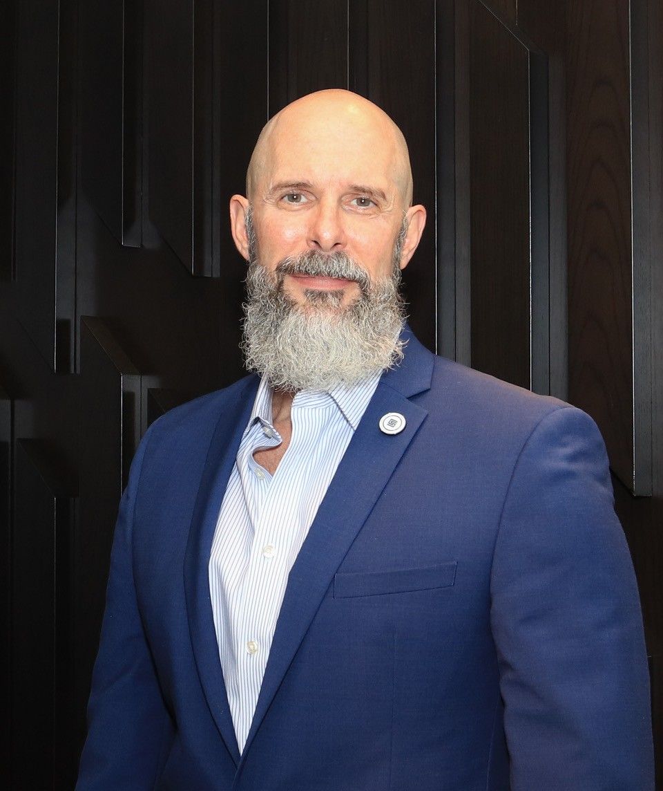 A bald man with a beard is wearing a blue suit.