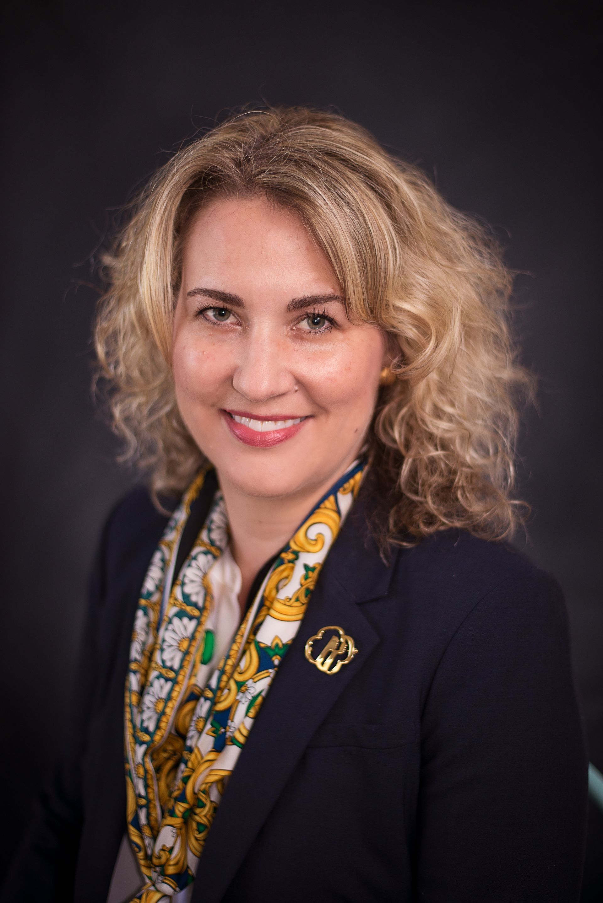 A woman in a suit and scarf is smiling for the camera.