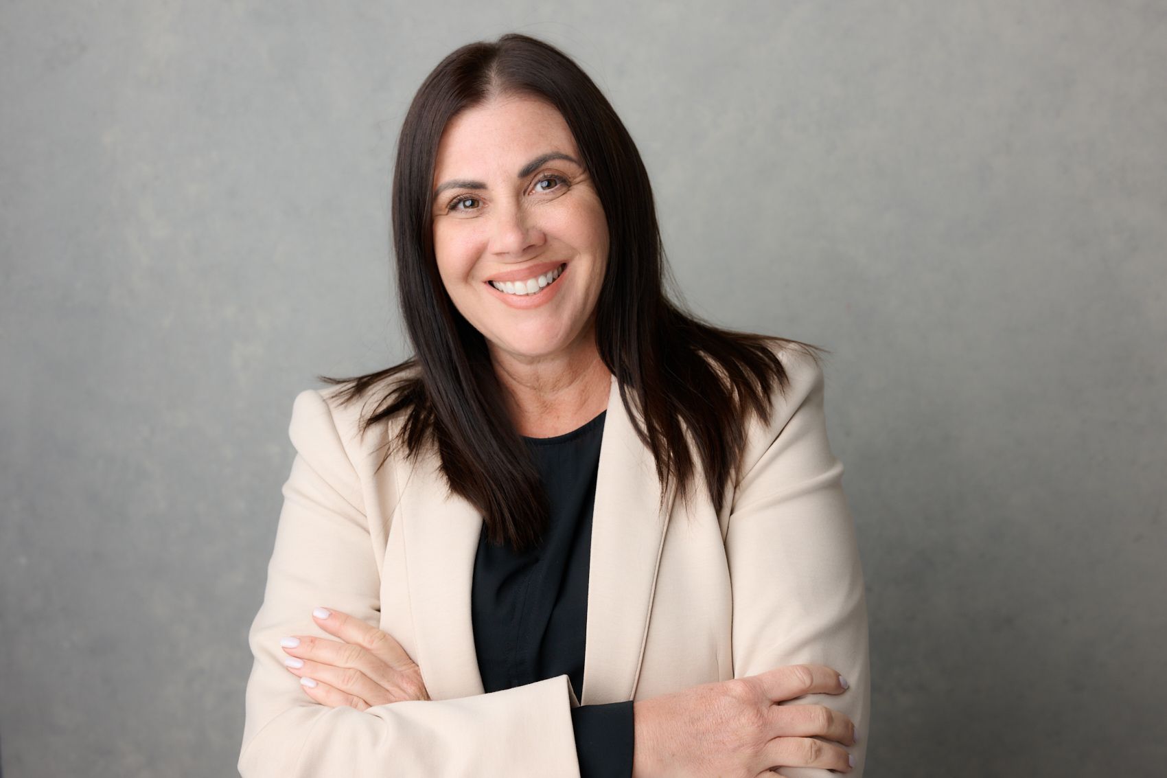 A woman in a white jacket is smiling with her arms crossed.