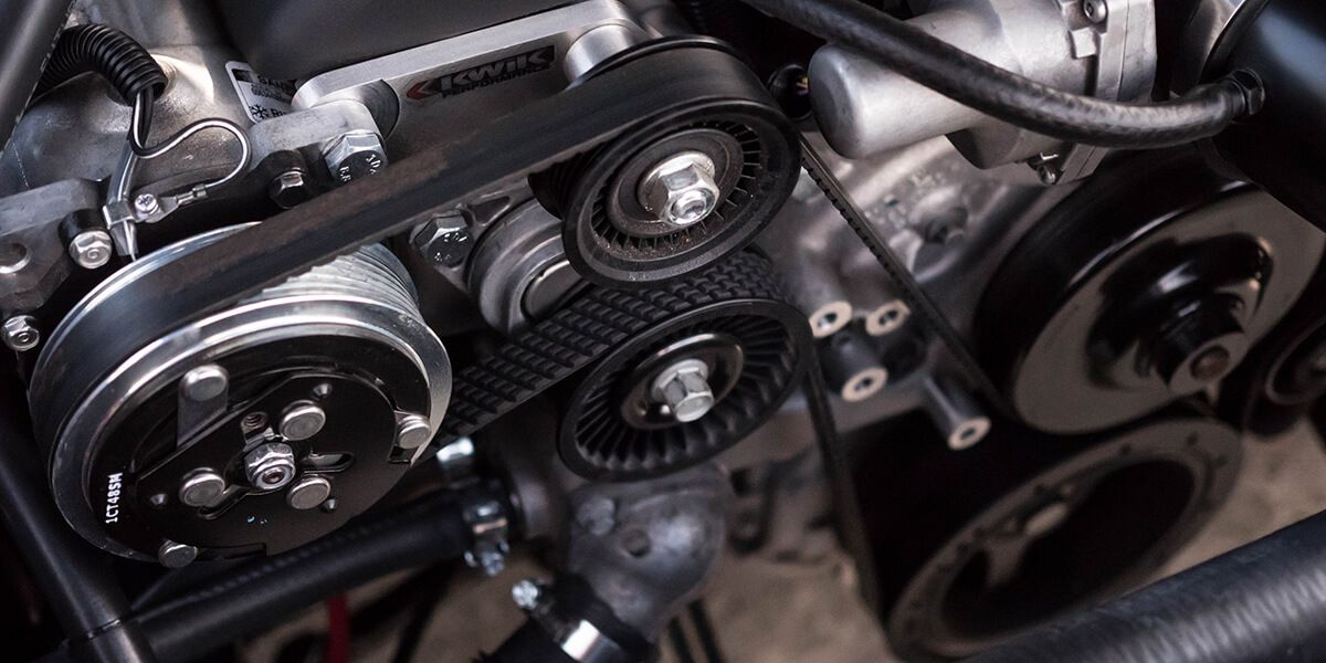 Primer plano de la correa de accesorios y las poleas del motor de un automóvil, debajo del capó.