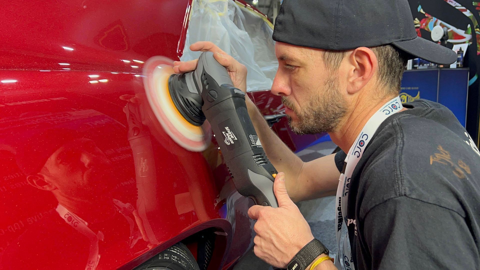 Man polishing a red car panel with a buffing tool in a workshop
