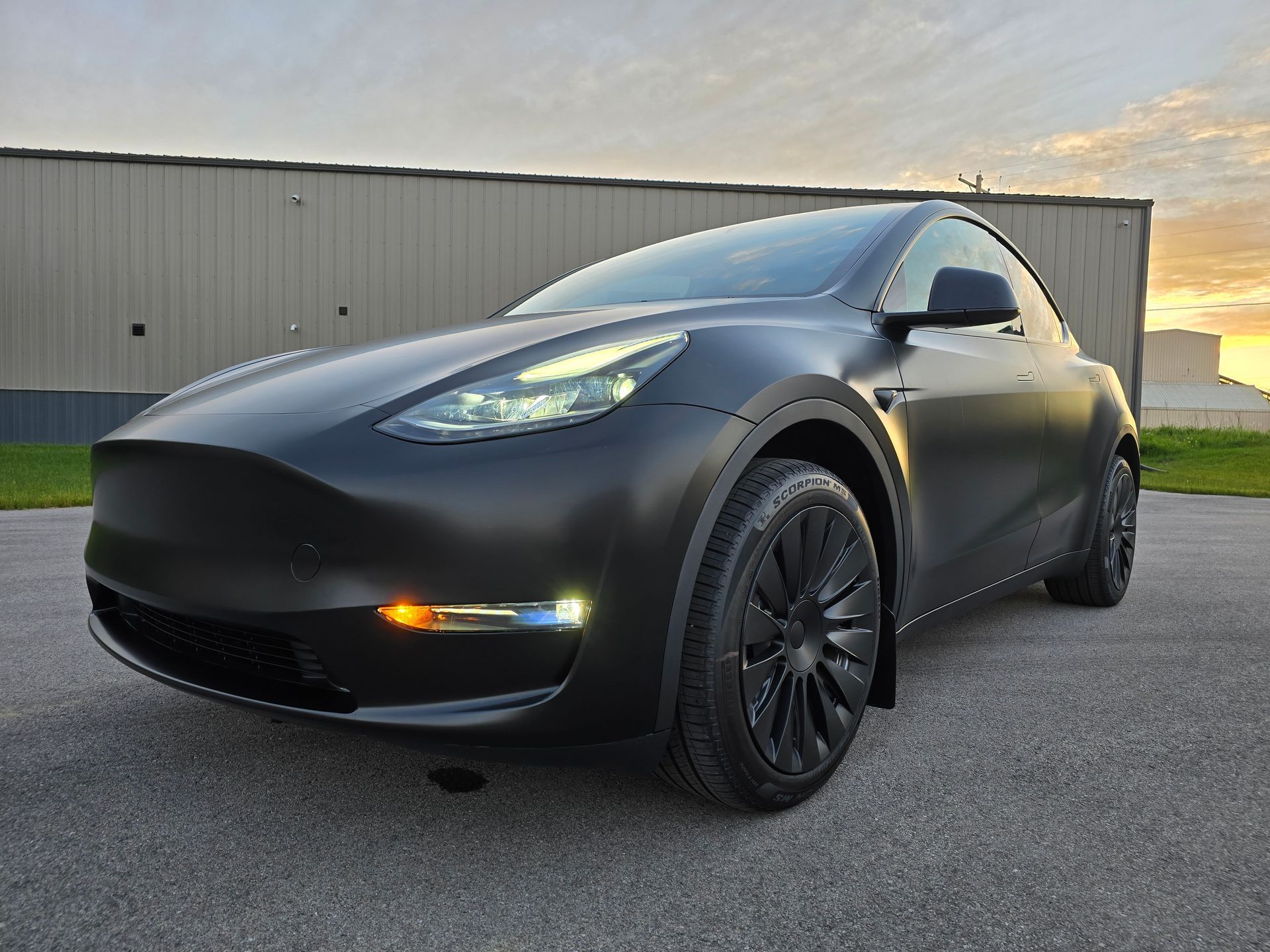Black Tesla parked on pavement beside a warehouse at sunset