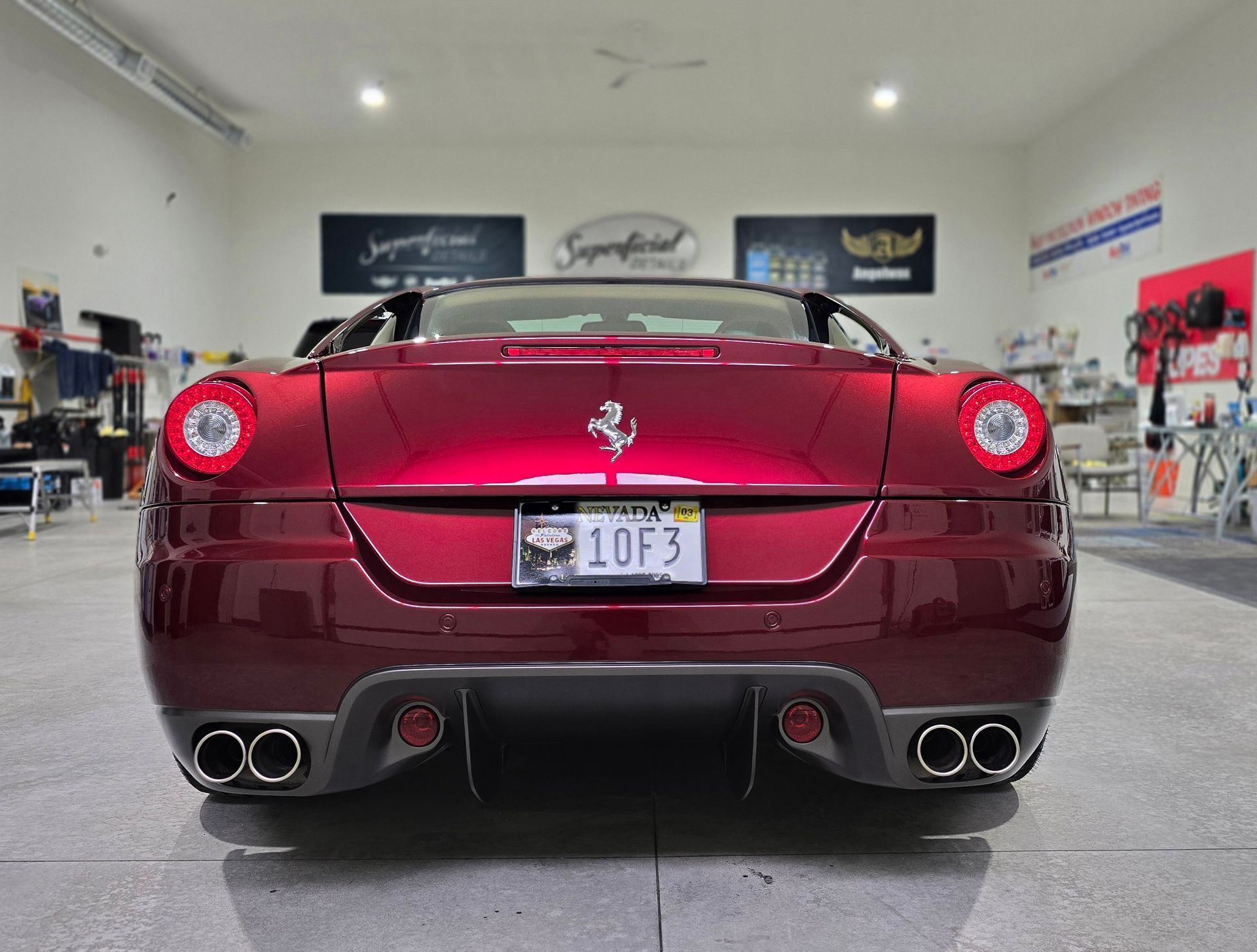 Rear view of a red Ferrari sports car parked indoors, showing quad exhausts and a custom license plate.