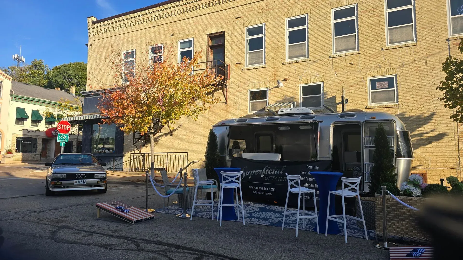 Outdoor café seating beside a brick building and parked car on a sunny street corner