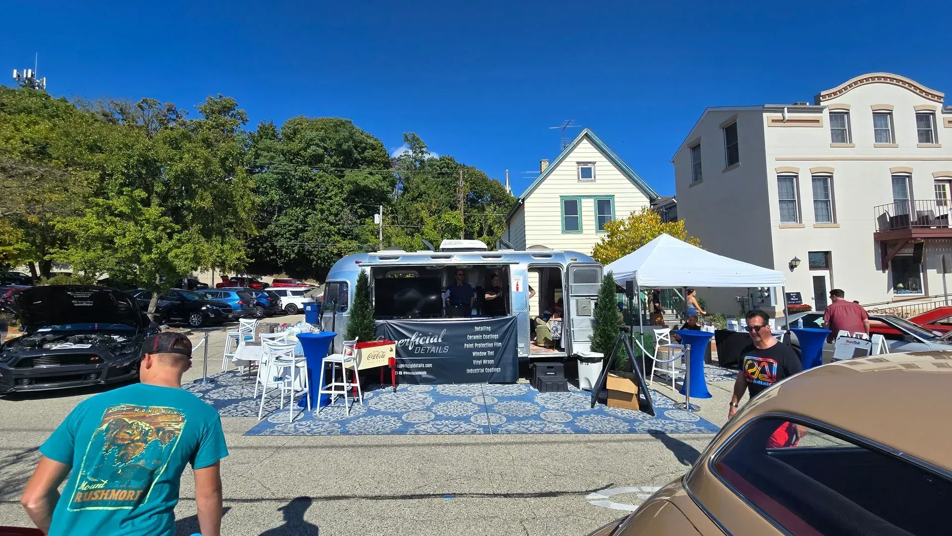 Outdoor market with a food truck, people browsing, and vendor tents in front of colorful buildings.