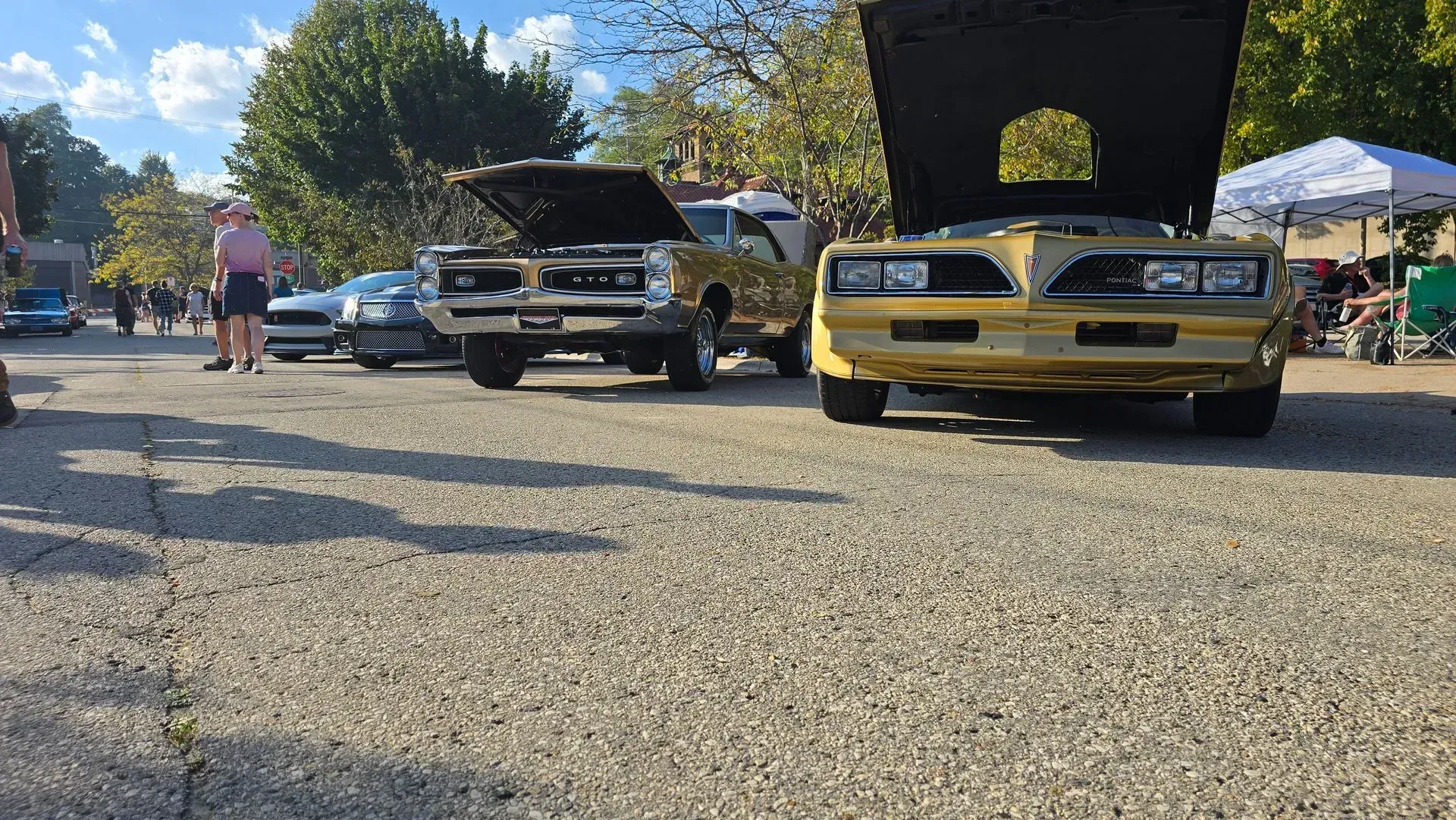 Classic cars with open hoods on display at an outdoor car show under a sunny sky