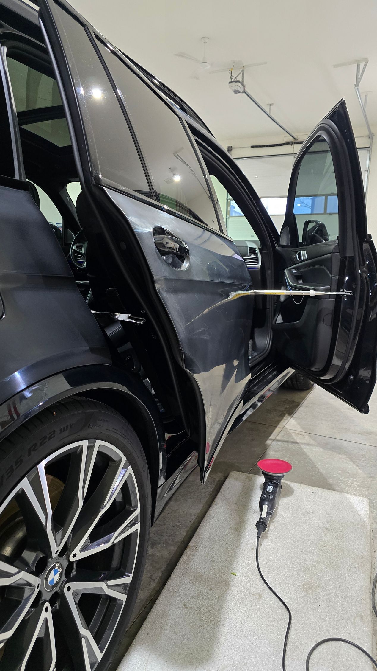 Hands polishing a red car’s front fender with a buffer near the headlight