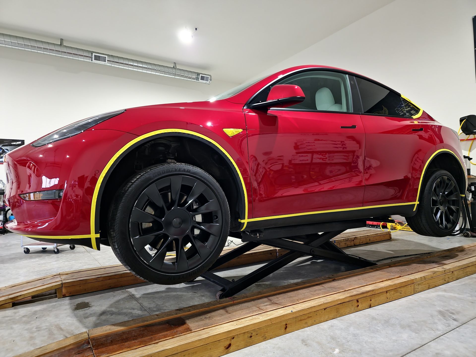 Red Tesla-style sports car on a car lift in a white garage, side view