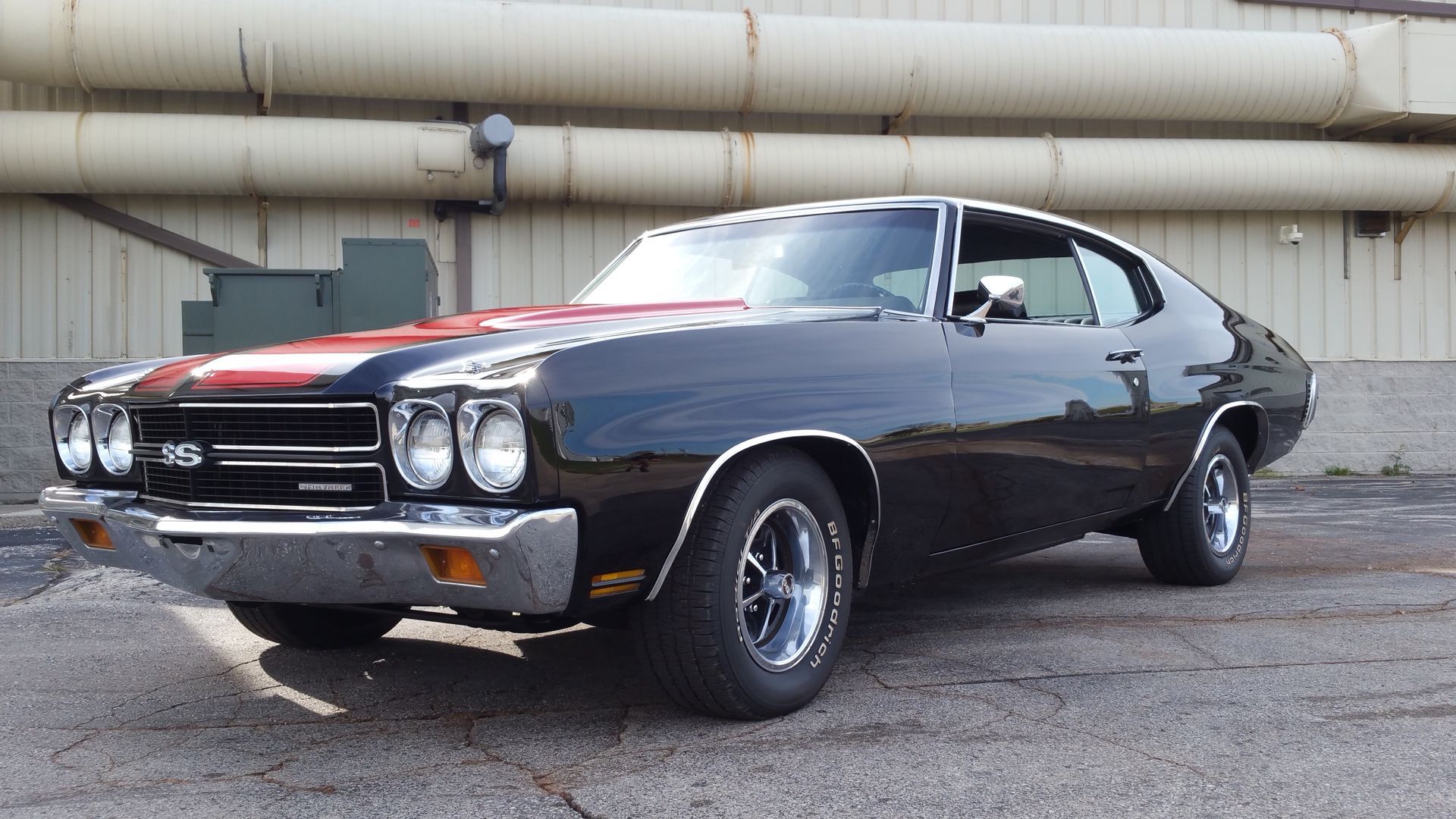 Classic black muscle car parked outdoors beside a large industrial building.