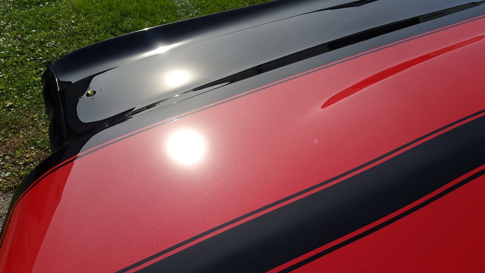 Close-up of a red car roof with black spoiler and bright sun reflection