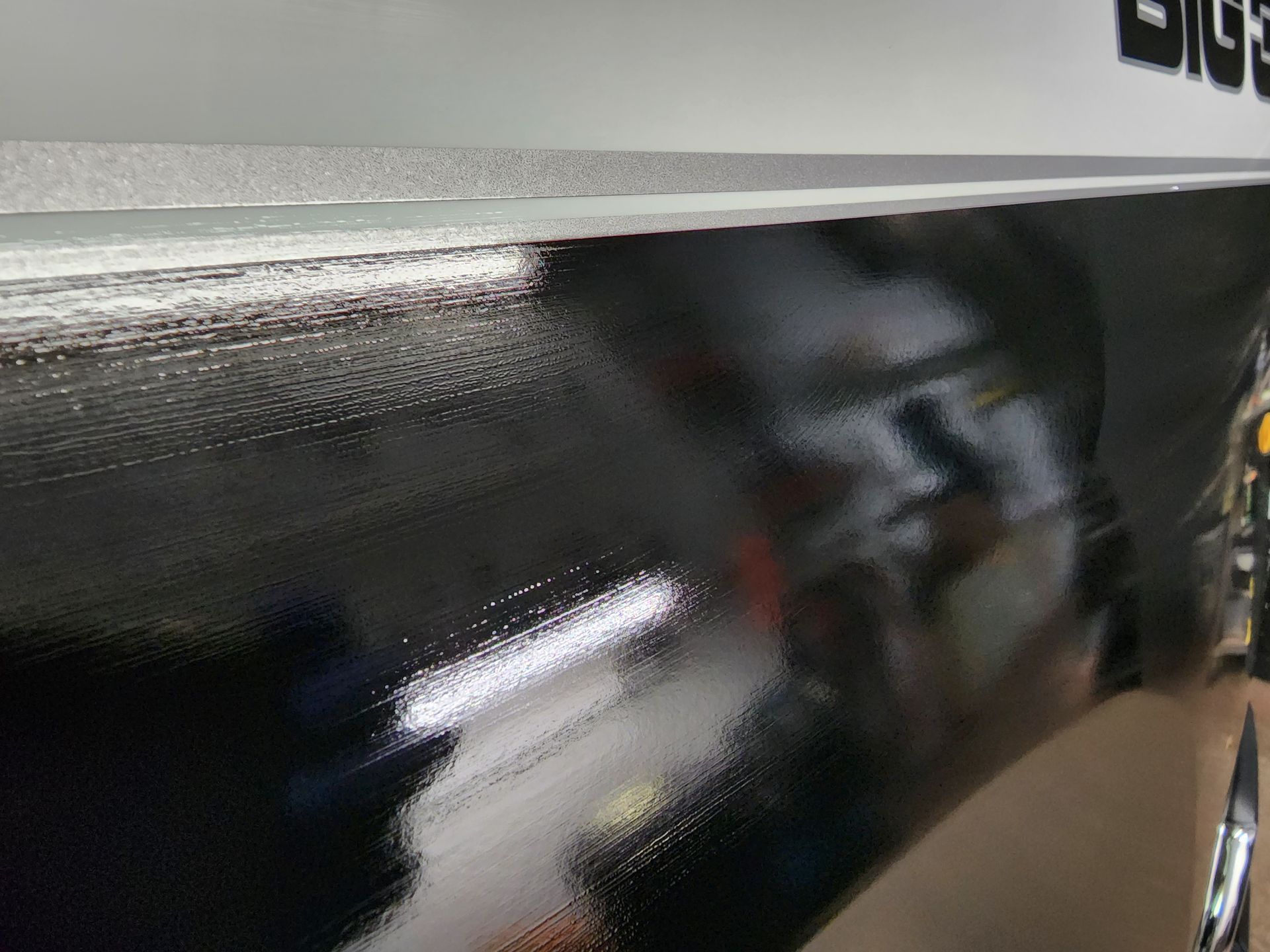 Close-up of a glossy black car side panel reflecting the surroundings