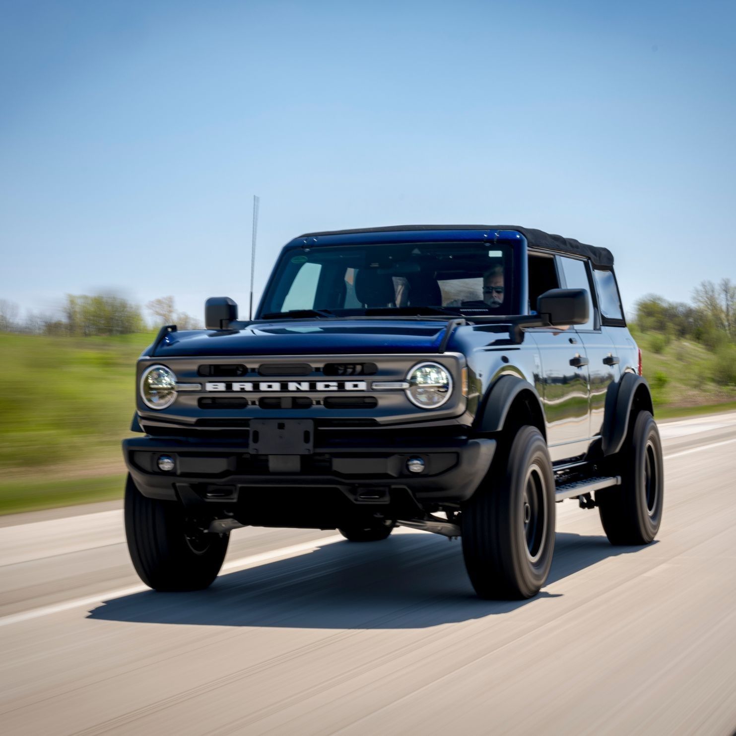 Black Ford Bronco convertible driving on a road under a clear blue sky