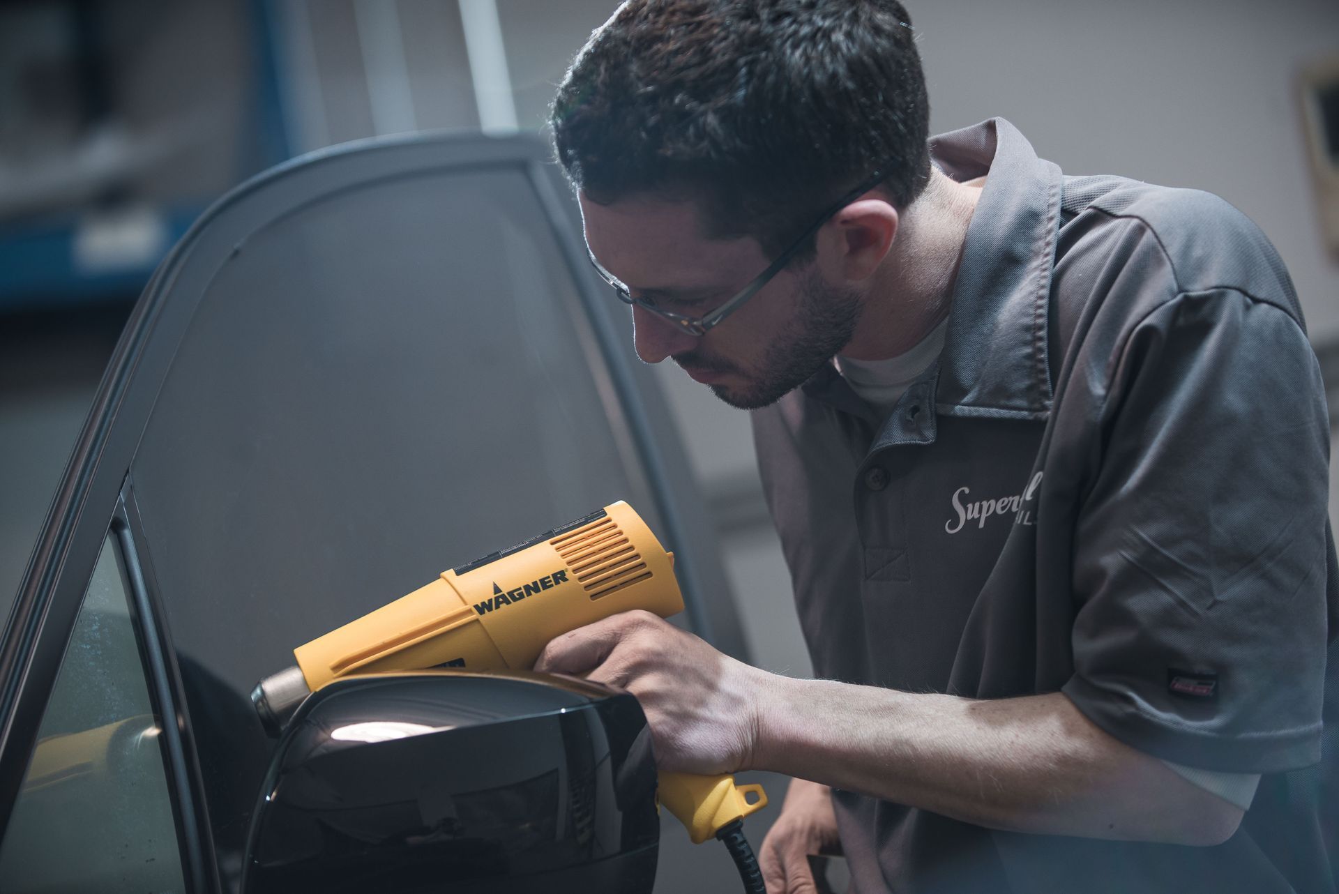 Man using a yellow heat gun to repair a car’s side mirror outdoors