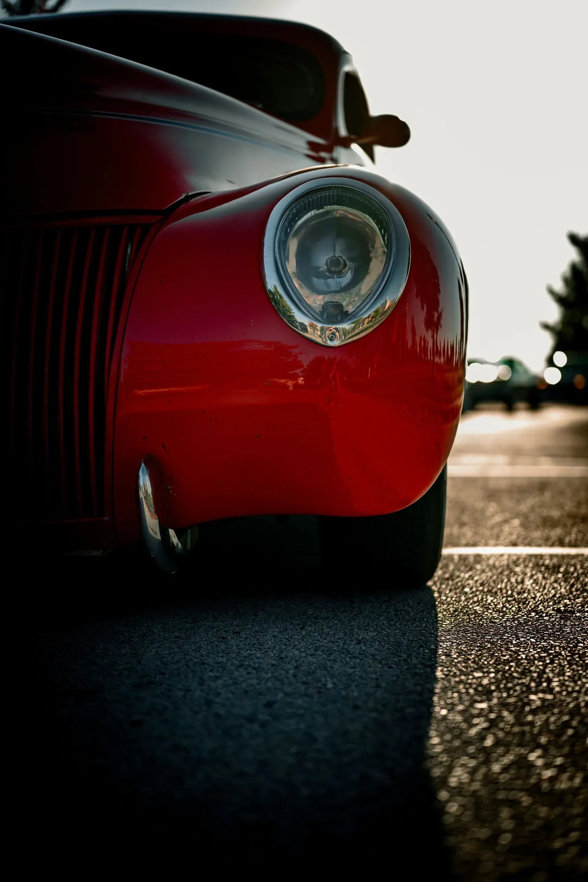 Close-up of a red classic car’s rear wheel and tail light on a sunlit road.