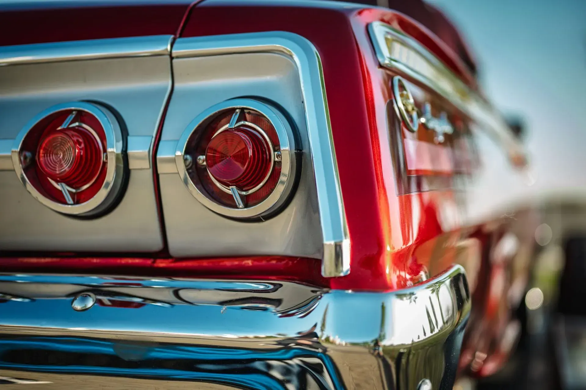 Close-up of a red classic car’s chrome rear with round taillights outdoors