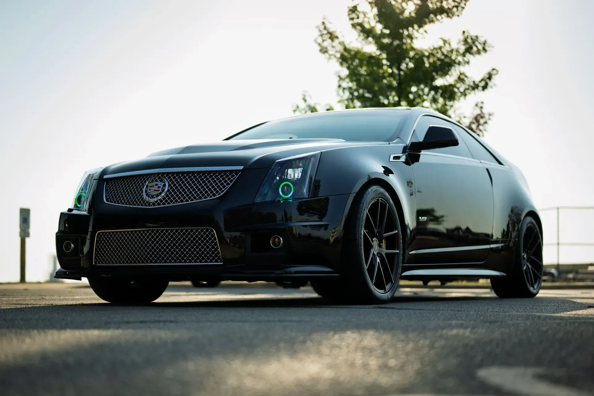 Black Cadillac coupe parked outdoors on a road, low-angle view against a bright sky