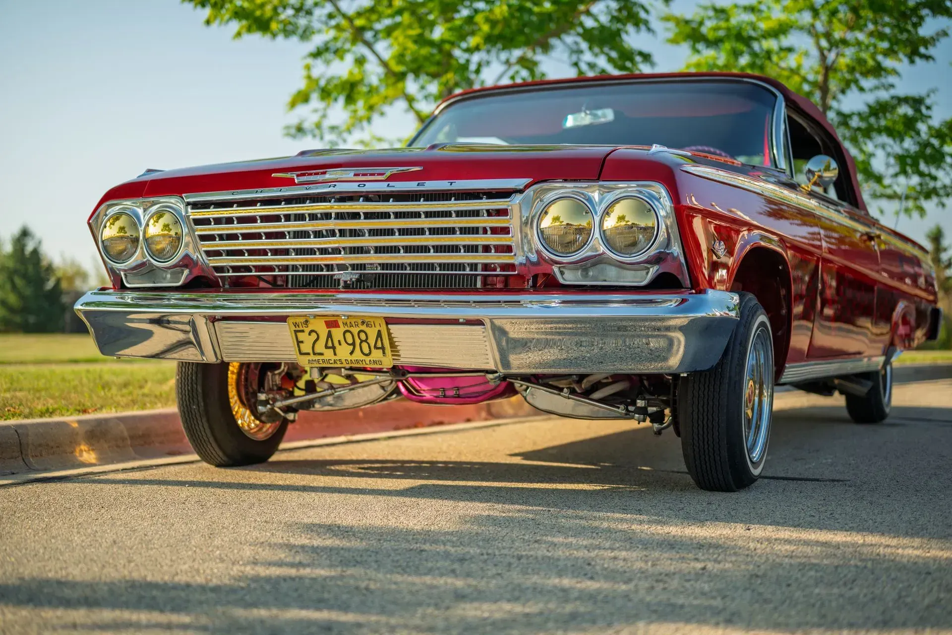 Red classic car parked outdoors on a sunny day, low-angle front view.