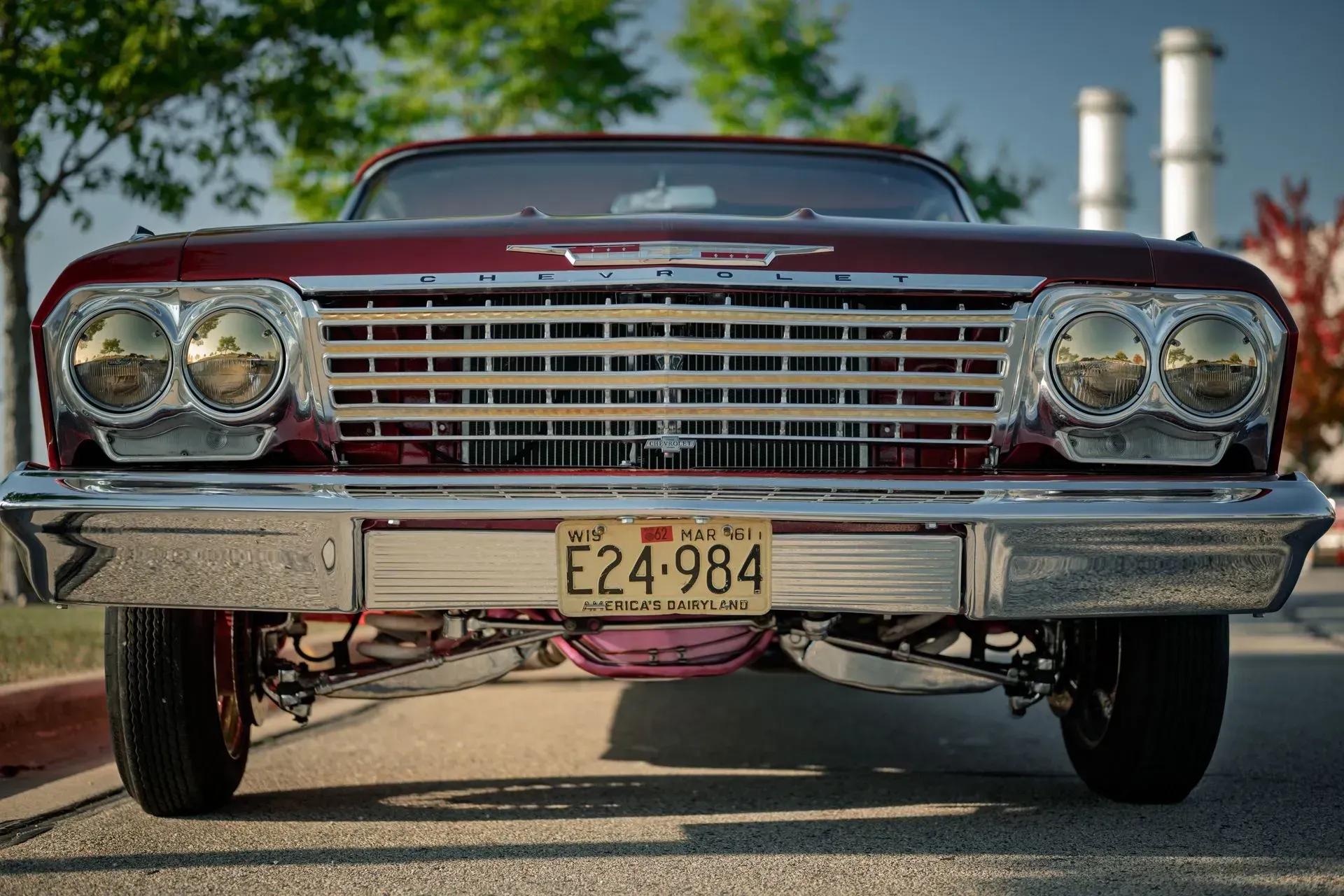 Front view of a red classic car with chrome grille and headlights, parked outdoors with a visible license plate.