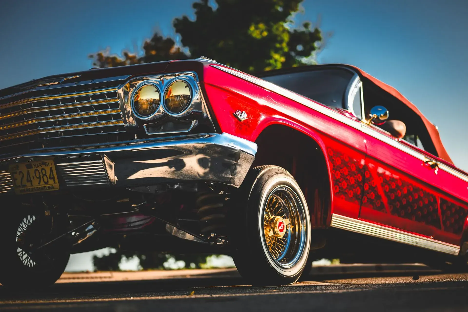 Low-angle view of a red classic car with chrome details and whitewall tires driving on a road