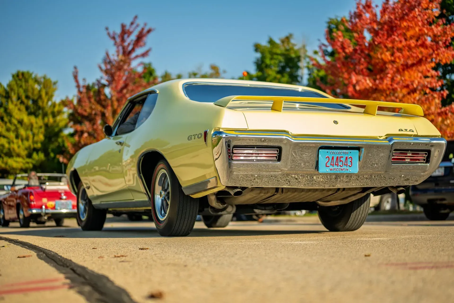 Yellow classic muscle car parked on a road with autumn trees in the background