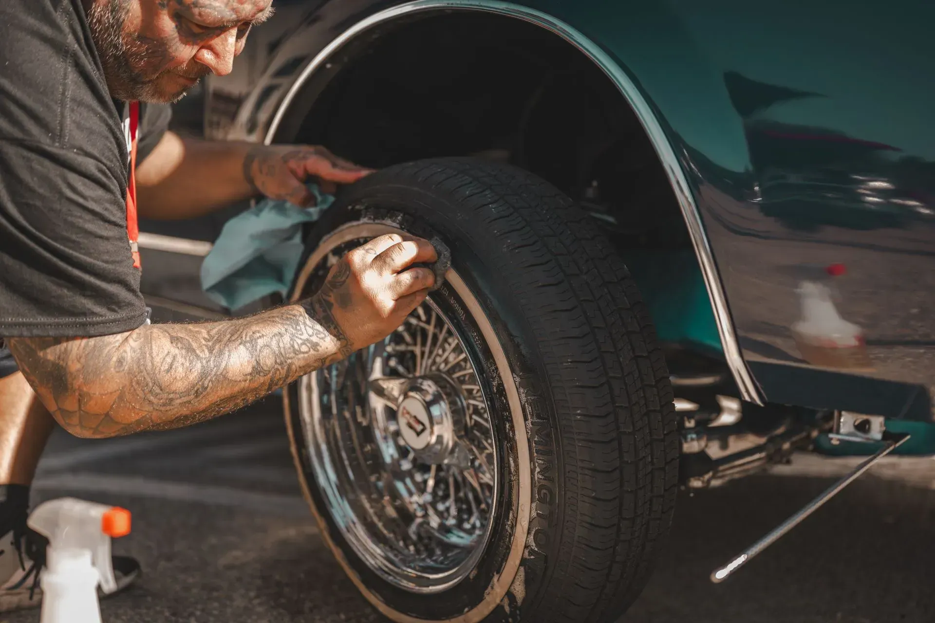 Mechanic polishing a car wheel rim beside a dark green vehicle