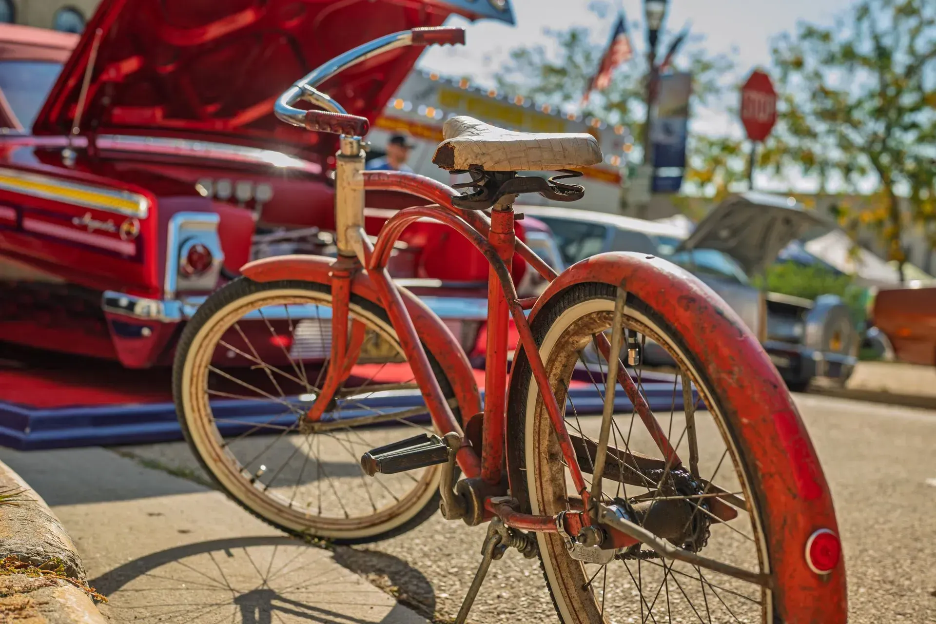 Red vintage bicycle parked beside a classic red car at an outdoor car show