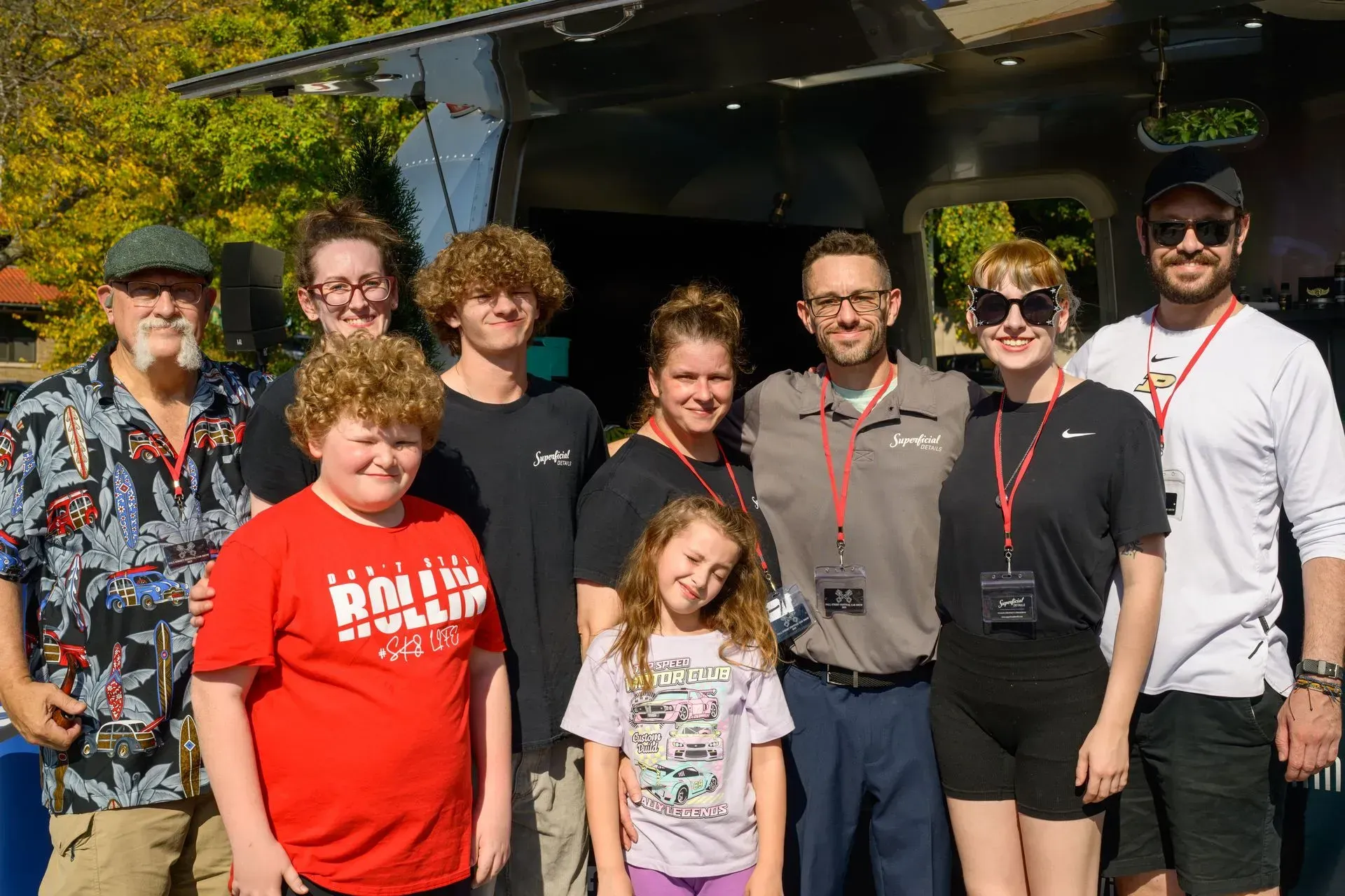 Group of people standing outdoors in bright sunlight, smiling at the camera.