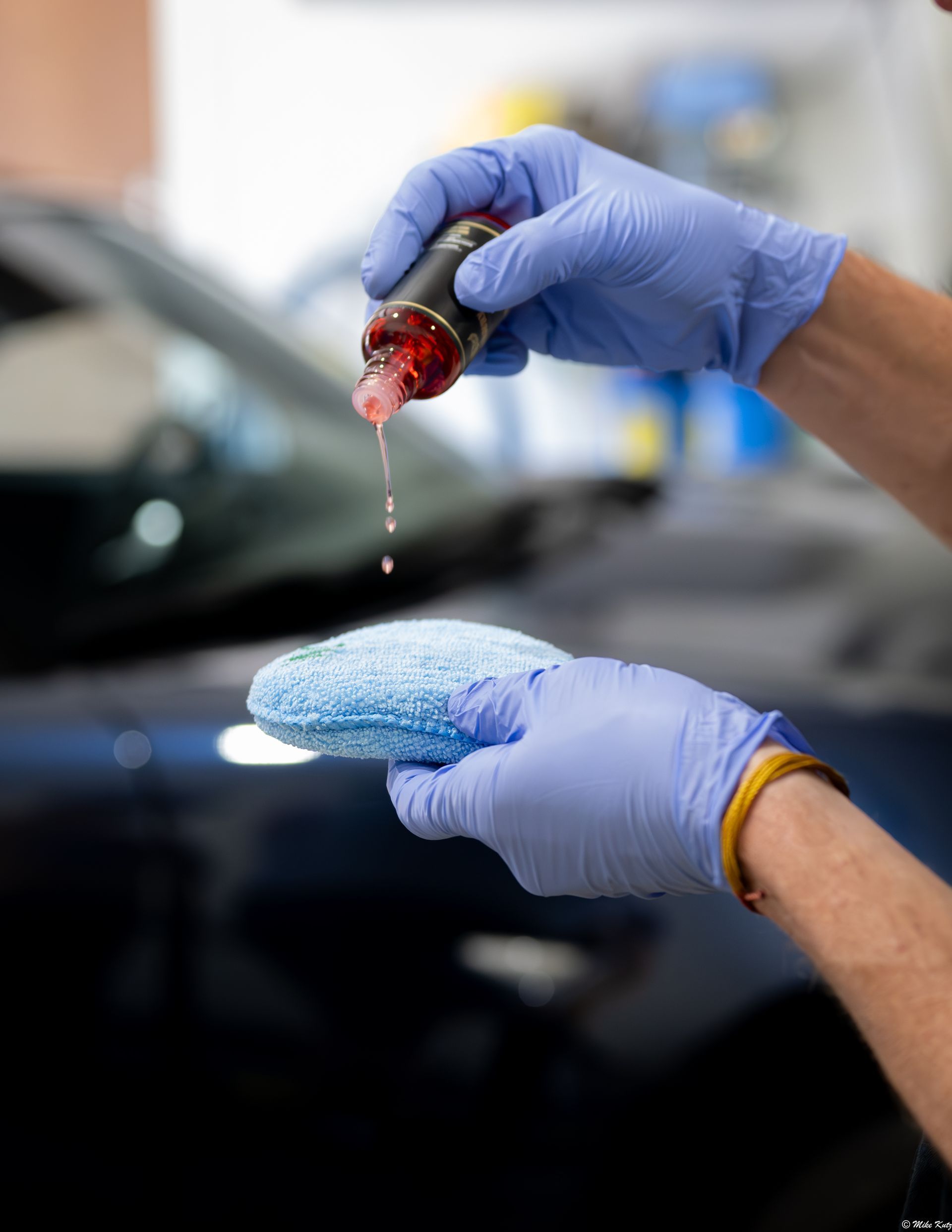 Gloved hands applying red fluid to a blue absorbent pad over a black car body