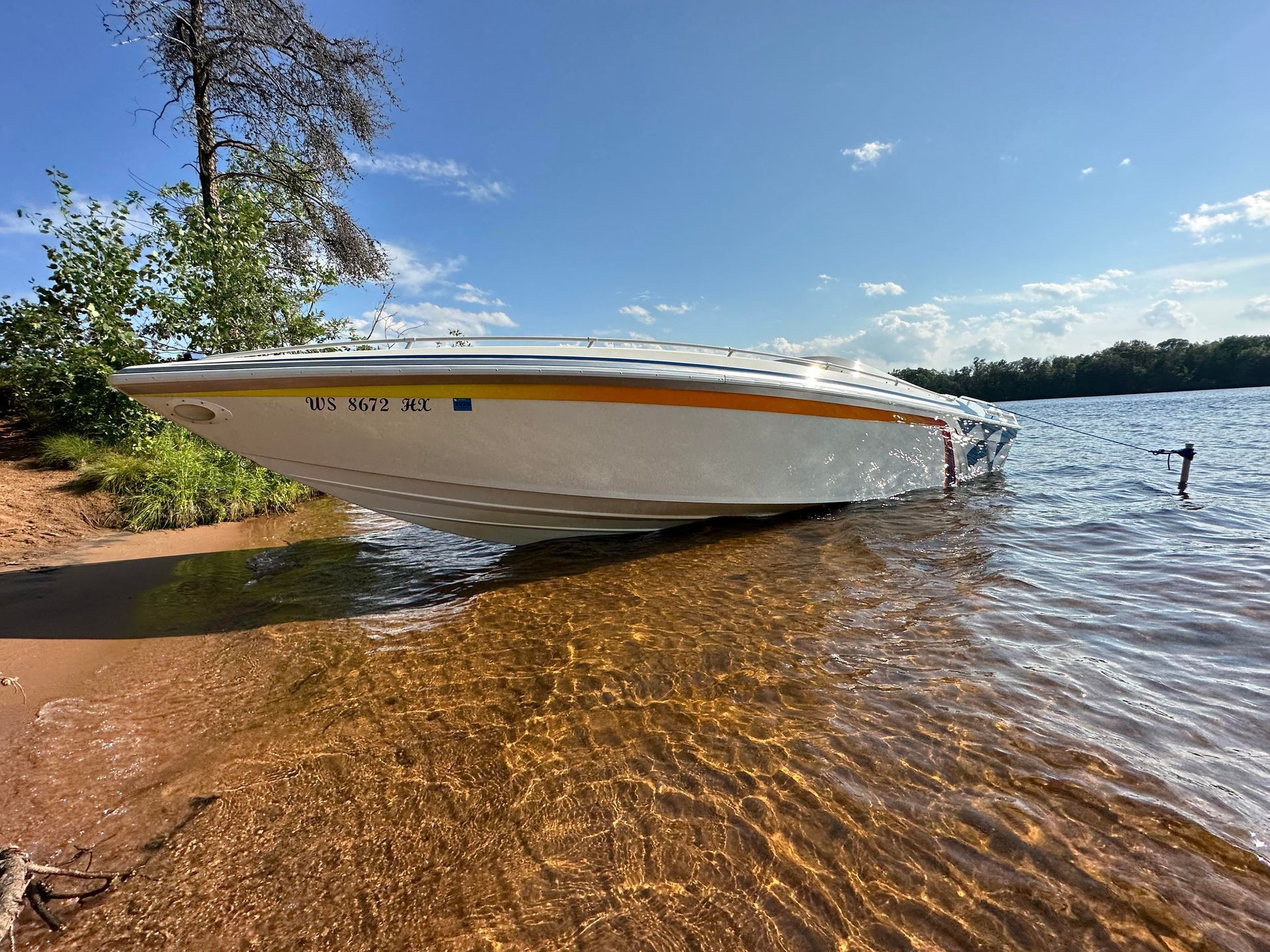 White speedboat pulled up on a sandy lakeshore under a clear blue sky, with rippling water nearby