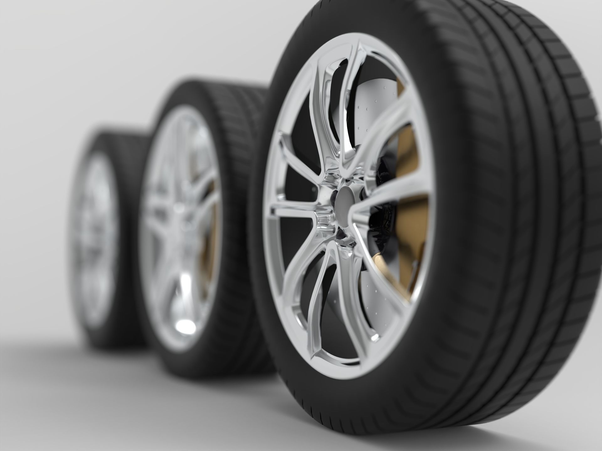 Three chrome car wheels with black tires on a light gray background
