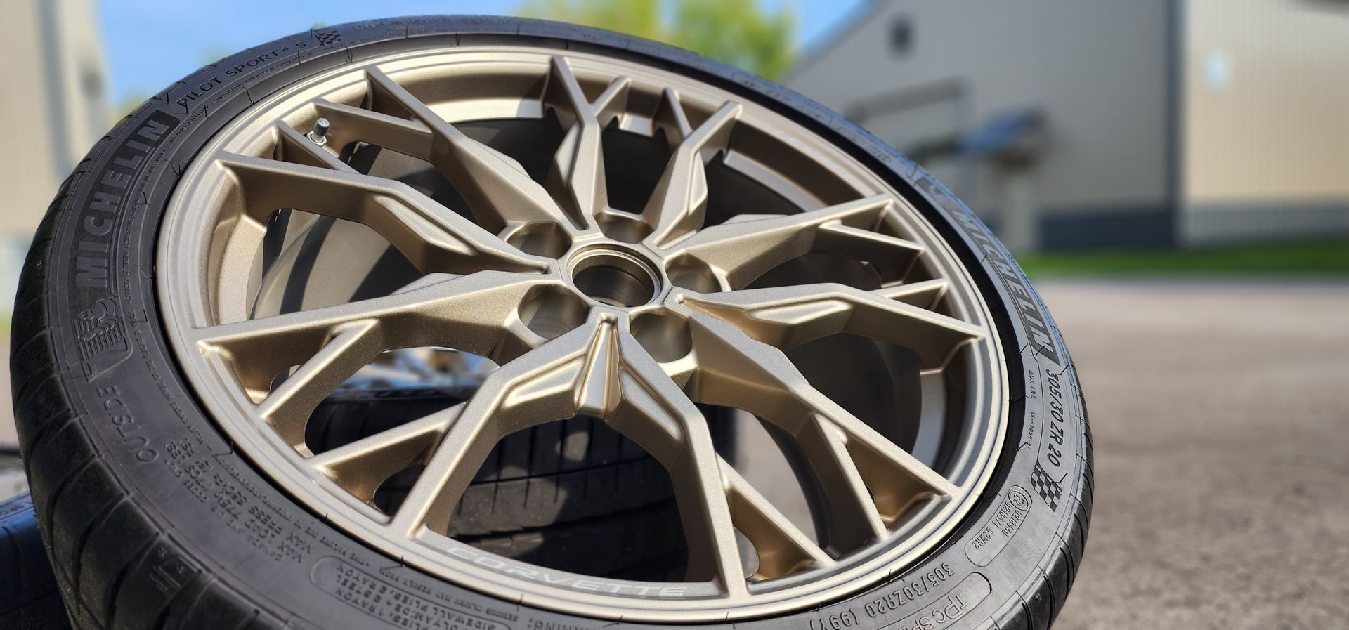 Close-up of a bronze alloy car wheel and tire resting on pavement outdoors