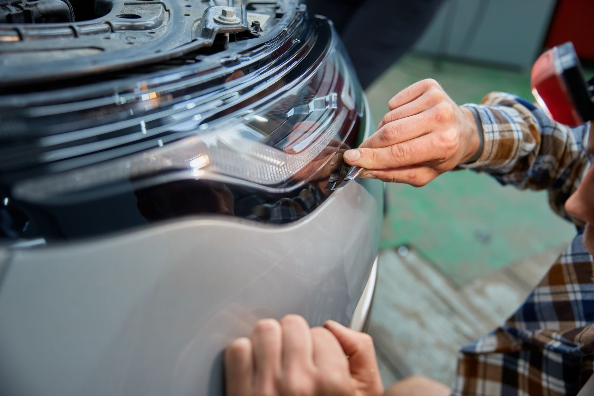 Hands applying vinyl wrap to a car bumper in a garage
